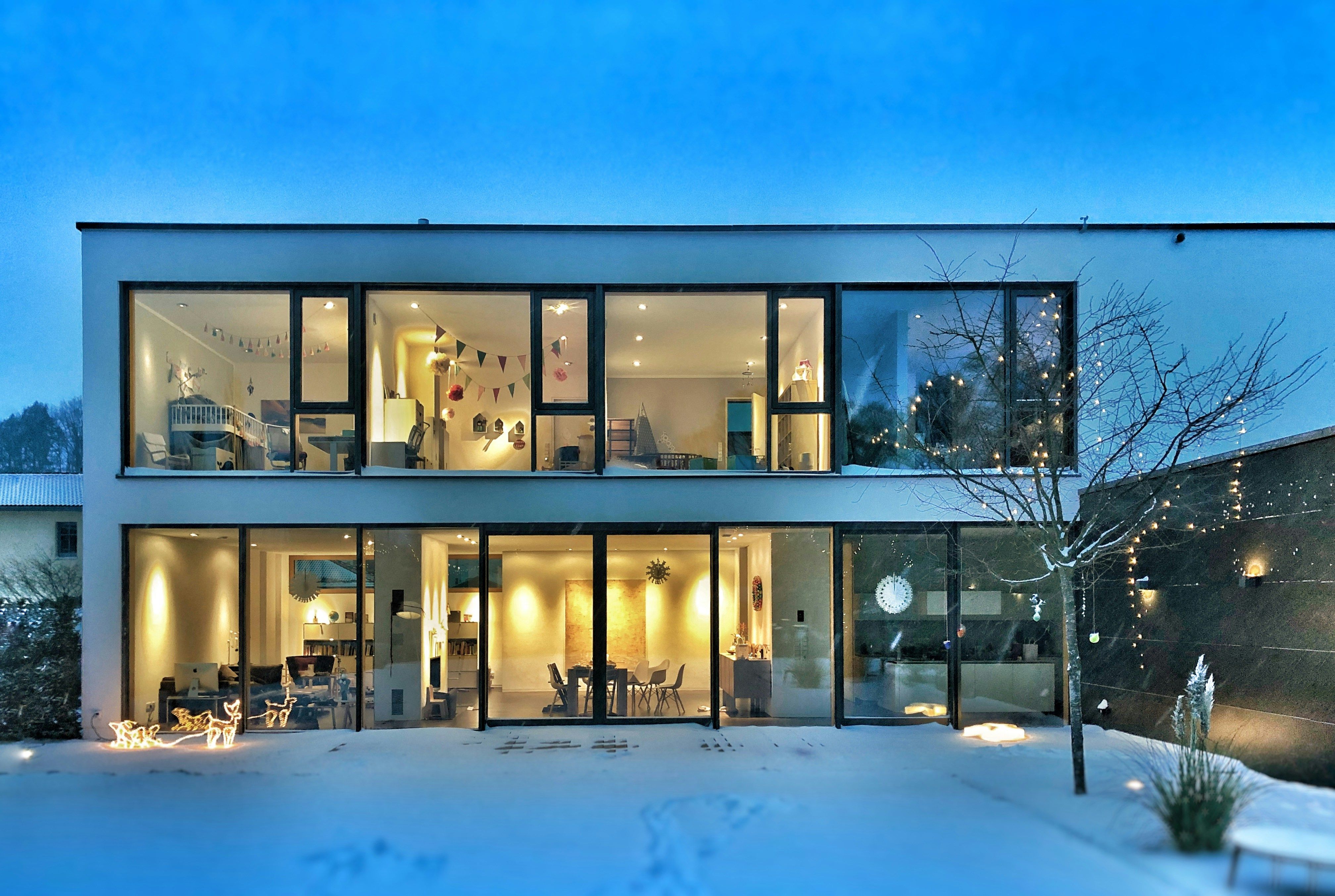 Modern villa i KL-trä med stora glaspartier i vinterskrud, fotograferad i skymning